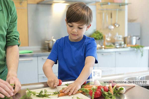 Junge schneidet Gemüse in der Küche