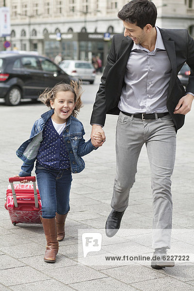 Girl pulling a trolley bag while running with her father
