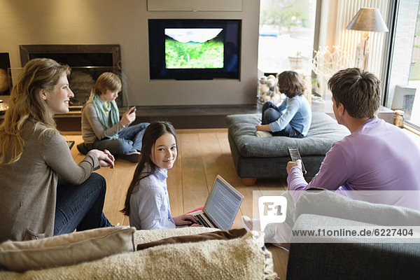 Familie mit elektronischen Geräten im Wohnzimmer