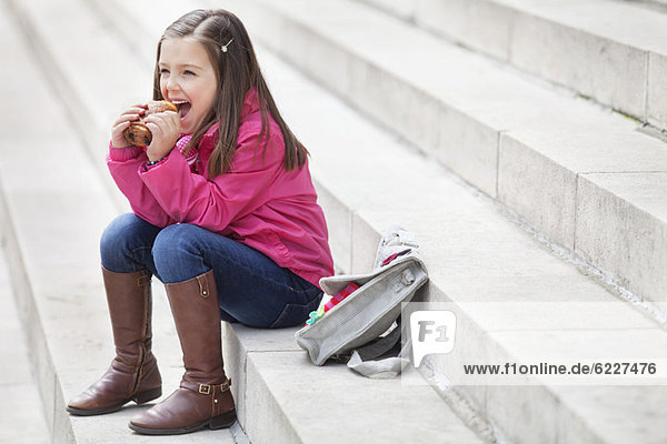 Schoolgirl sitting on the steps and eating pain au chocolat