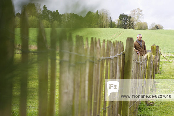 Mann steht am Zaun auf einem Feld