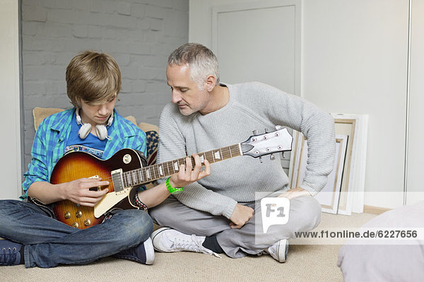 Teenage boy learning guitar with his father at home