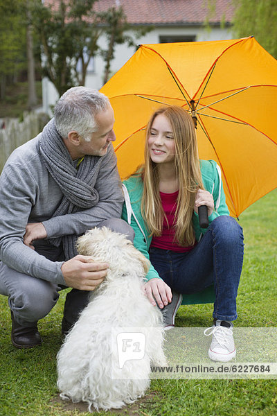 Mann mit seiner Tochter beim Verwöhnen eines Hundes im Rasen