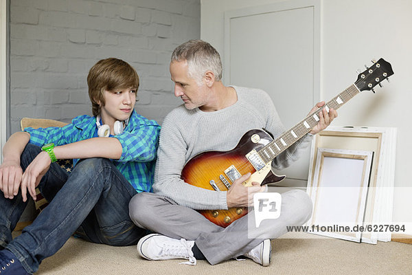 Mann  der mit seinem Sohn zu Hause Gitarre spielt.