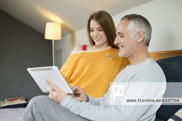 Mann  der ein digitales Tablett mit seiner Tochter zu Hause benutzt.