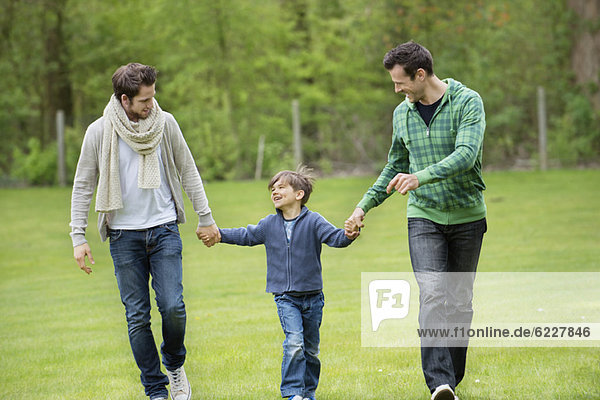 Junge  der mit zwei Männern in einem Park spazieren geht.