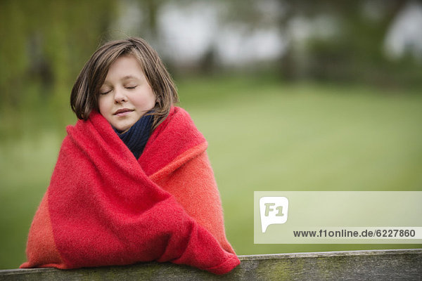 Mädchen in einer Decke mit geschlossenen Augen auf einem Bauernhof.