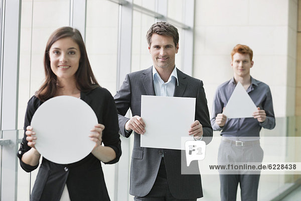 Business executives holding geometrical shaped placards in an office