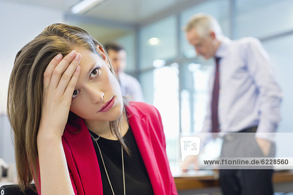 Female executive looking sad in an office with her colleagues discussing in the background