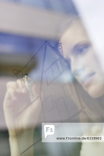 Geschäftsfrau beim Zeichnen eines Hauses auf einer Glasfläche