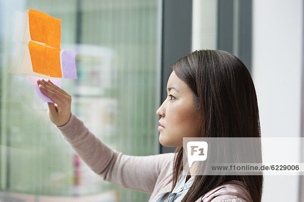 Geschäftsfrau klebt Notizzettel auf Glas im Büro