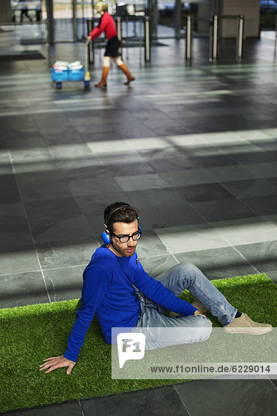 Businessman relaxing on grass and listening to music in an office lobby