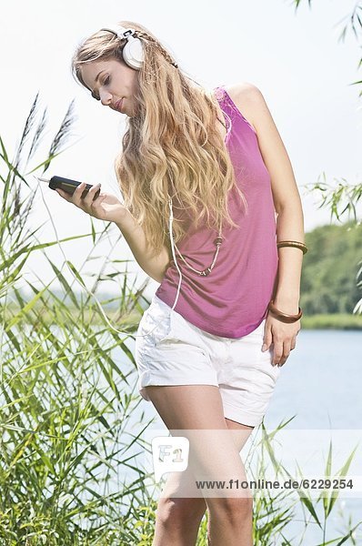 Blonde junge Frau hört Musik an einem See