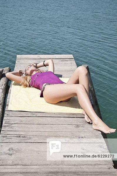 Blonde junge Frau liegt auf einem Steg am See