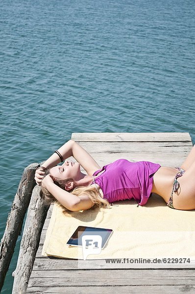 Blonde junge Frau liegt auf einem Steg am See