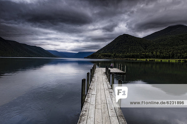 Frau sitzt bei düsterer Wetterstimmung am Ende eines Holzstegs  Lake Rotoroa  Südinsel  Neuseeland