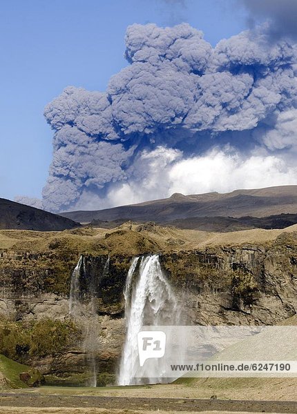 Distant view of the Seljalandsfoss waterfall with the ash plume of the Eyjafjallajokull eruption in the distance near Hella southern Iceland Iceland Polar Regions