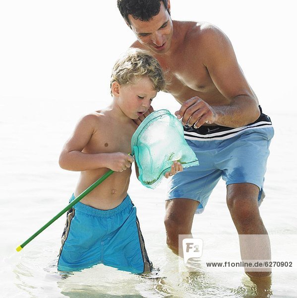 Father and son (6-8) in the surf holding fishing pole