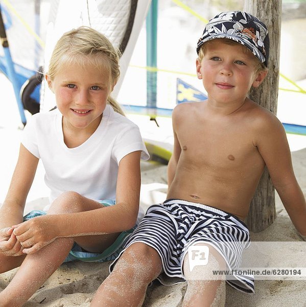 Boy and girl (6-8) on beach by windsurfer