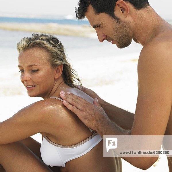 Man applying suncream to woman's back on beach