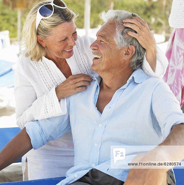 senior couple on beach on sunloungers