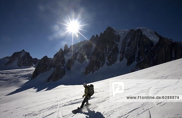 A snowboarder enjoys superb spring snow high on the famous Valley Blanche ski run  one of the world's most celebrated glacier descents  with Mont Blanc Du Tacul in the distance  Mont Blanc  Chamonix  western Alps  France  Europe
