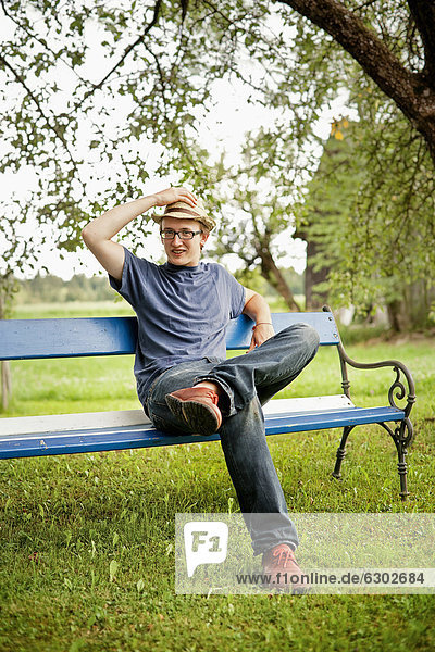 Junger Mann sitzt auf einer Bank im Garten
