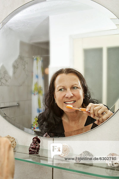 Frau beim Zähneputzen vor dem Spiegel im Badezimmer