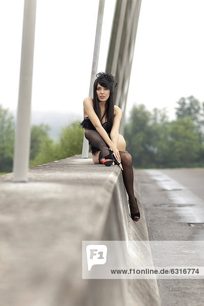 Young woman wearing black lingerie from La Perla and high-heeled shoes posing on a bridge