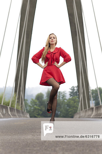Young woman in short red dress and high-heels posing on a bridge
