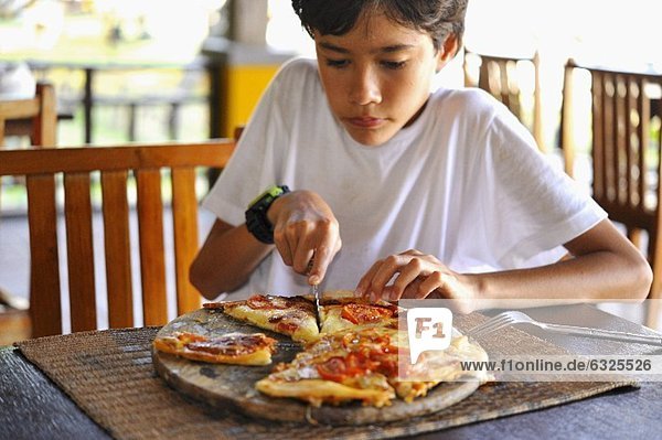 Junge schneidet Pizza in Portionen