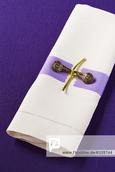 Weisse Leinenserviette mit Serviettendeko auf einer violetten Leinentischdecke