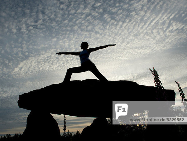 Silhouette der Frau in Krieger-Yoga-Pose auf einem Felsen