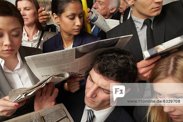 Businesspeople reading newspapers on crowded train