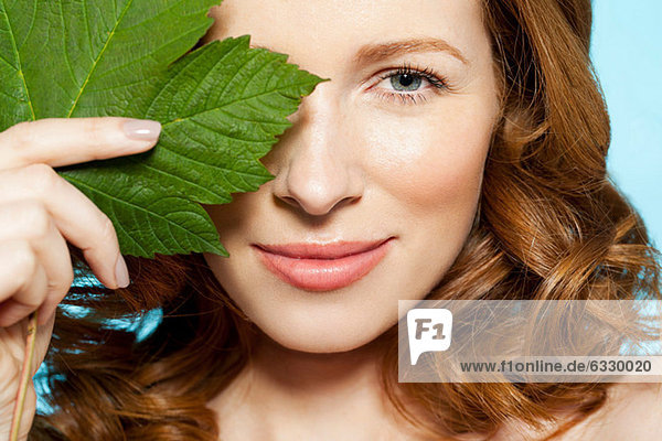 Woman covering eye with green leaf