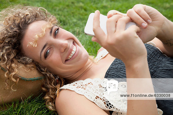 Junge Frau auf Rasen liegend mit Smartphone