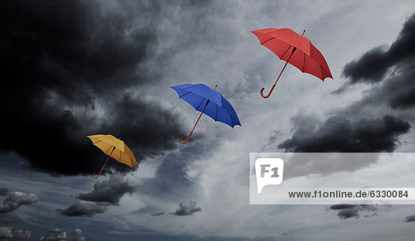 Three umbrellas floating through cloudy sky