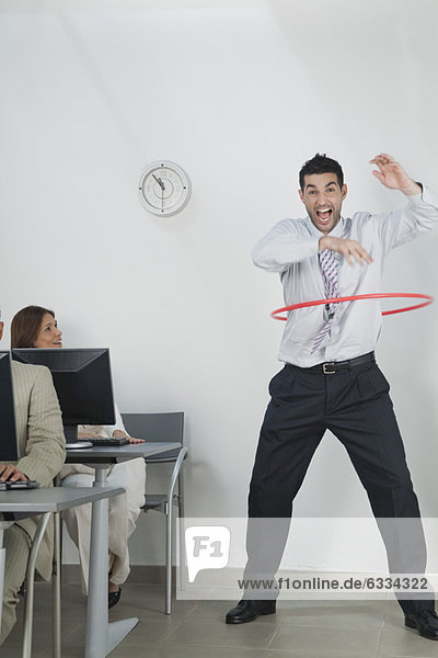 Young businessman playing with hula hoop in office