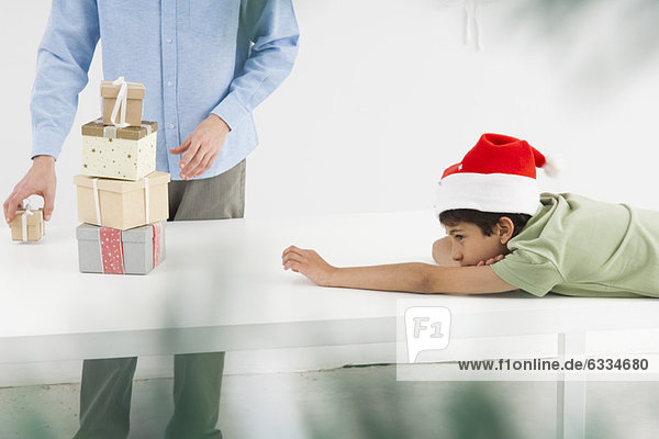 Boy looking longingly at stack of Christmas presents