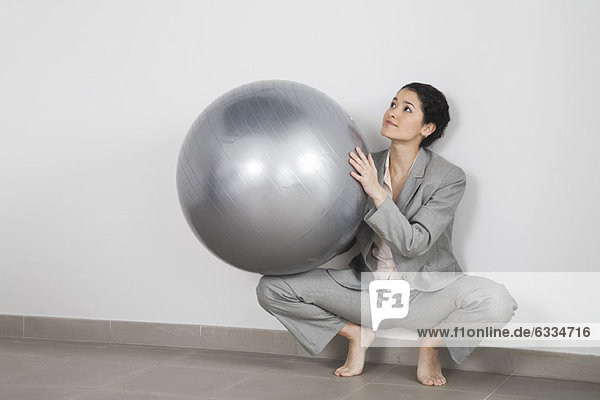 Junge Geschäftsfrau kauert gegen die Wand und hält den Fitnessball.