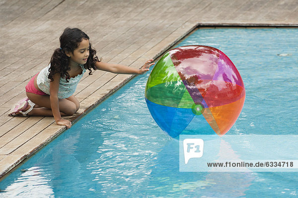 Girl crouching beside pool  playing with beach ball