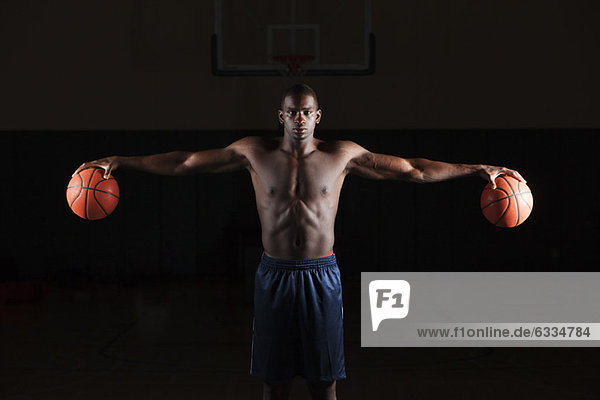 Barechested basketball player holding basketballs in both hands