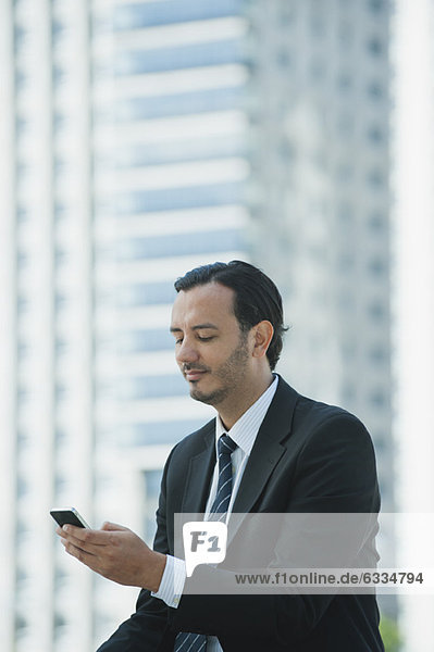 Business executive text messaging with cell phone outdoors