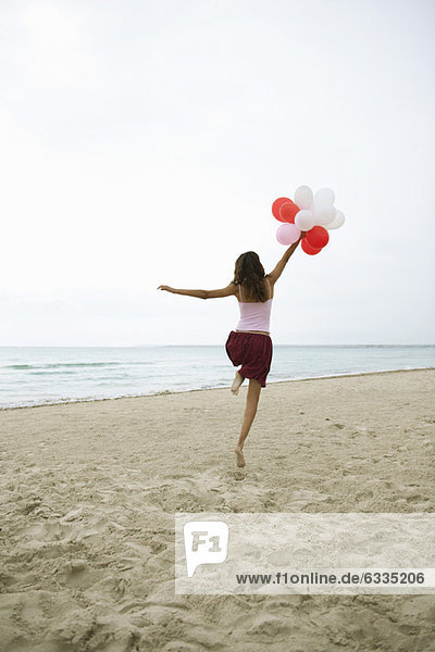 Frau läuft am Strand mit Luftballons  Rückansicht