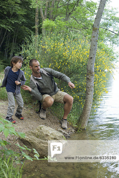 Vater und Sohn werfen Kieselsteine in den Fluss