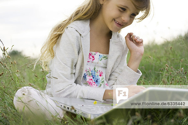 Girl sitting in grass  using laptop computer