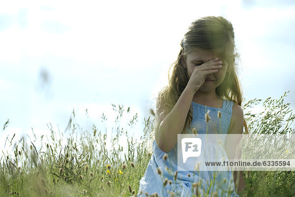 Girl crying in field  hand rubbing eyes