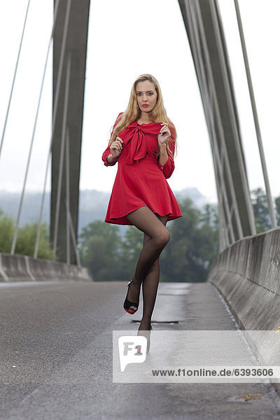 Young woman in a short red dress and high heels posing on a bridge