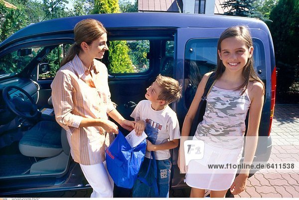 Eine Mutter steht mit ihren Kindern vor ihrem Auto