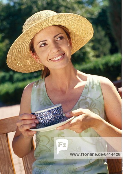 Eine Frau sitzt im Garten und trinkt Kaffee